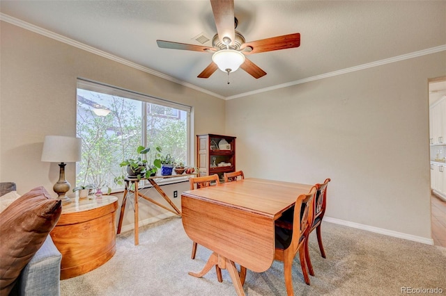 dining room featuring light colored carpet, a ceiling fan, ornamental molding, and baseboards