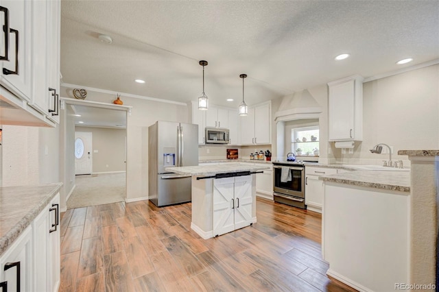 kitchen with appliances with stainless steel finishes, a sink, white cabinets, light wood finished floors, and a center island