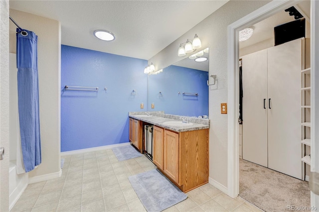 full bath with double vanity, a shower with shower curtain, a textured ceiling, and baseboards
