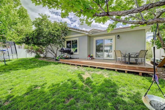 rear view of property with a wooden deck, stucco siding, a trampoline, and a tile roof