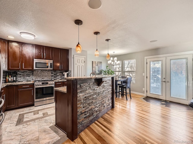 kitchen featuring appliances with stainless steel finishes, light stone counters, dark brown cabinets, decorative light fixtures, and a notable chandelier