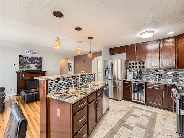 kitchen featuring appliances with stainless steel finishes, light stone counters, beverage cooler, sink, and hanging light fixtures