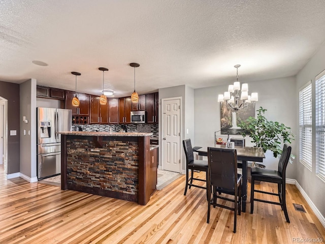 kitchen featuring tasteful backsplash, hanging light fixtures, appliances with stainless steel finishes, and an inviting chandelier