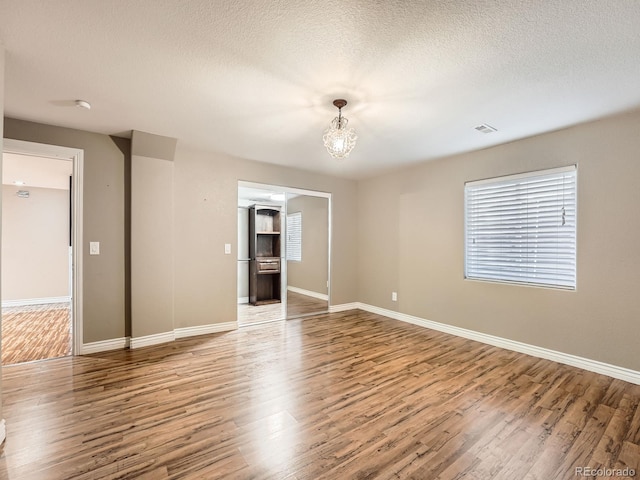 unfurnished room featuring a chandelier, wood-type flooring, and a textured ceiling