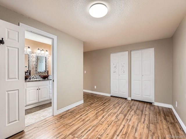 unfurnished bedroom featuring multiple closets, ensuite bathroom, light hardwood / wood-style floors, and a textured ceiling