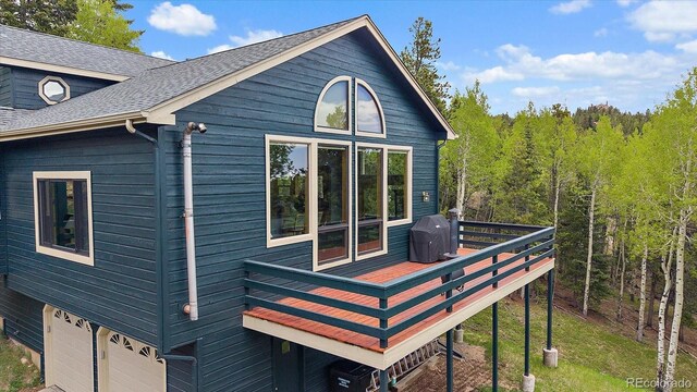 11222 Conifer Mountain Rd, Conifer, CO 80433 - view of property exterior with a wooden deck, a garage, a shingled roof, and a forest view