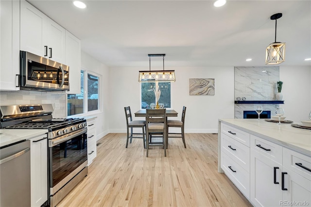 kitchen with white cabinets, stainless steel appliances, light hardwood / wood-style flooring, and hanging light fixtures