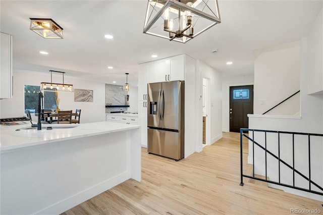 kitchen with light stone countertops, light wood-type flooring, decorative light fixtures, stainless steel fridge with ice dispenser, and white cabinetry