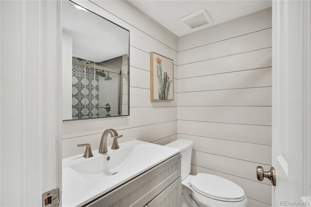 bathroom with vanity, toilet, a tile shower, and wooden walls