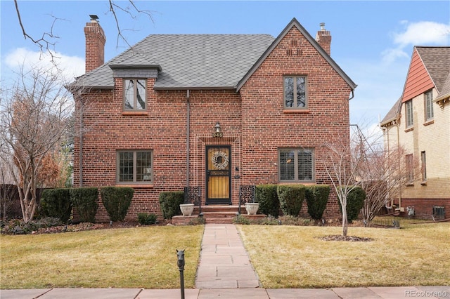 tudor home with a front yard, a chimney, and brick siding