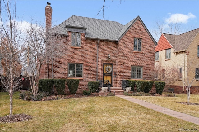 english style home featuring brick siding, a chimney, and a front yard