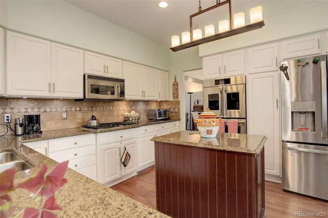 kitchen with light stone countertops, appliances with stainless steel finishes, decorative backsplash, white cabinets, and hanging light fixtures