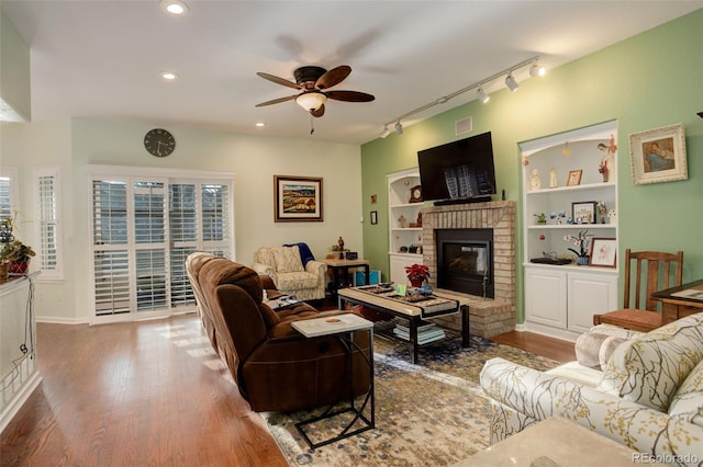 living room with ceiling fan, a fireplace, rail lighting, and dark hardwood / wood-style floors