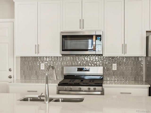 kitchen with white cabinetry, sink, light stone counters, backsplash, and appliances with stainless steel finishes