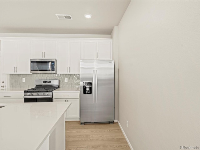 kitchen with decorative backsplash, light stone countertops, light wood-type flooring, stainless steel appliances, and white cabinetry