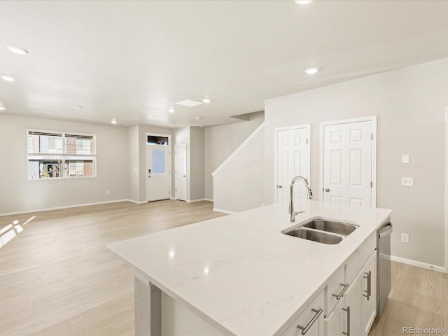 kitchen featuring a kitchen island with sink, sink, stainless steel dishwasher, light hardwood / wood-style floors, and light stone counters