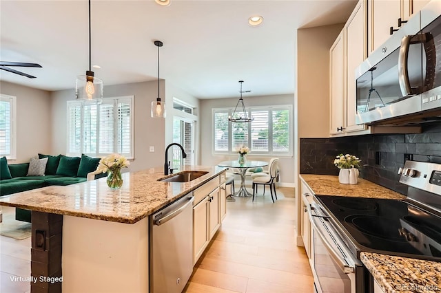 606 E Dry Creek Pl, Littleton, CO 80122 - kitchen featuring appliances with stainless steel finishes, light stone countertops, a kitchen island with sink, a ceiling fan, and tasteful backsplash