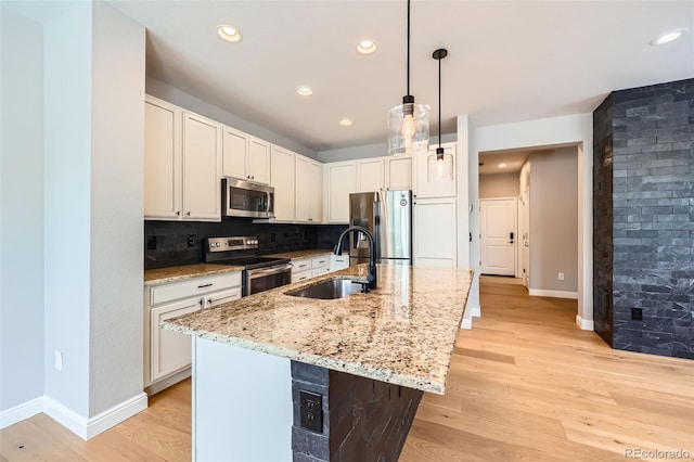 606 E Dry Creek Pl, Littleton, CO 80122 - kitchen featuring stainless steel appliances, light stone counters, light wood-style floors, hanging light fixtures, and a center island with sink