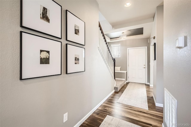 corridor with stairs, wood finished floors, baseboards, a tray ceiling, and recessed lighting
