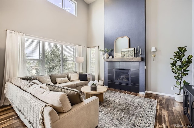living room featuring baseboards, a high ceiling, wood finished floors, and a tile fireplace