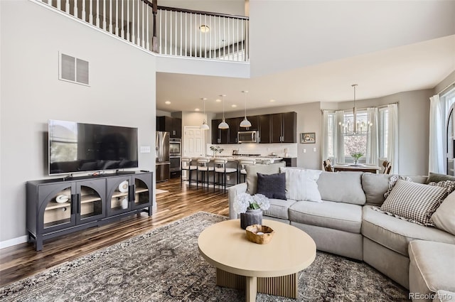living room with a high ceiling, a notable chandelier, dark wood-style floors, and visible vents