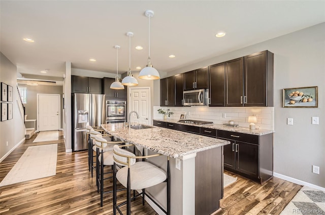kitchen featuring a kitchen bar, appliances with stainless steel finishes, wood finished floors, dark brown cabinets, and a sink