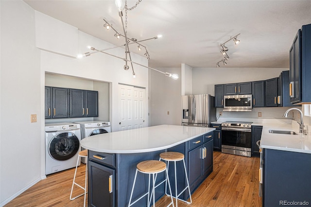 kitchen featuring sink, washing machine and dryer, blue cabinetry, appliances with stainless steel finishes, and a breakfast bar area