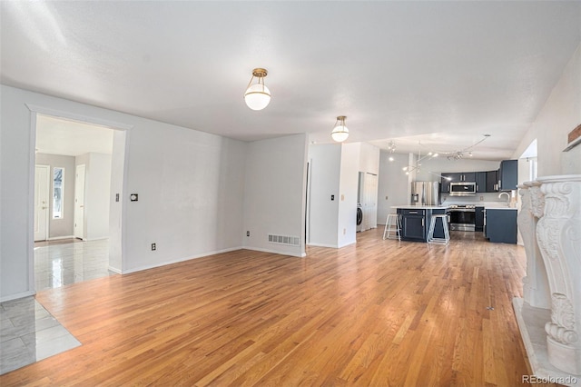 unfurnished living room with sink, rail lighting, light hardwood / wood-style floors, and washer / dryer