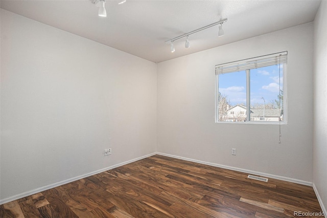 spare room with dark hardwood / wood-style flooring and track lighting