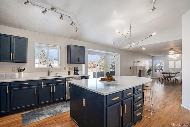 kitchen with sink, blue cabinets, light hardwood / wood-style floors, a breakfast bar area, and a kitchen island