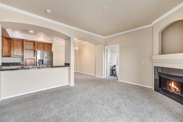 unfurnished living room with light colored carpet, ornamental molding, and a tiled fireplace