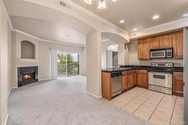 kitchen with a tile fireplace, light carpet, crown molding, and appliances with stainless steel finishes