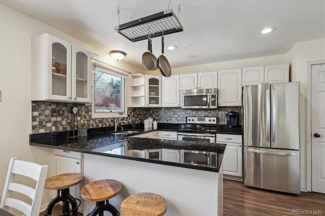 kitchen with appliances with stainless steel finishes, glass insert cabinets, a peninsula, white cabinetry, and a sink