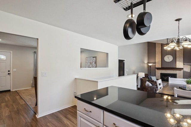 kitchen with dark countertops, a fireplace, dark wood finished floors, and baseboards