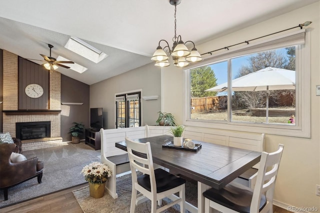 dining space featuring a healthy amount of sunlight, lofted ceiling with skylight, a fireplace, and wood finished floors