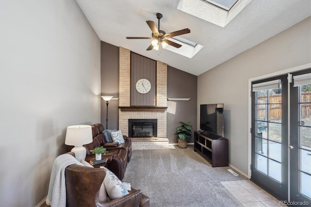 living area featuring ceiling fan, light tile patterned floors, light carpet, a skylight, and a brick fireplace