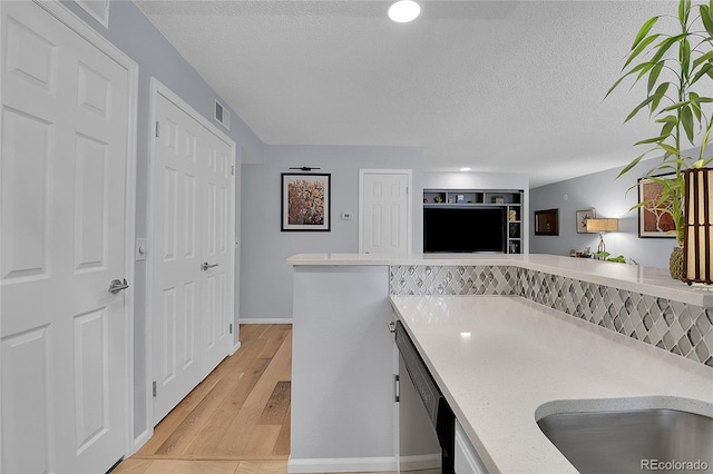 kitchen featuring dishwashing machine, kitchen peninsula, light wood-type flooring, and a textured ceiling