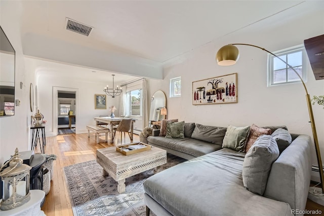 living room featuring an inviting chandelier, light wood-type flooring, and visible vents