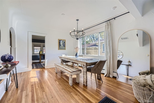 dining space with light wood-style floors, arched walkways, a baseboard radiator, and a chandelier