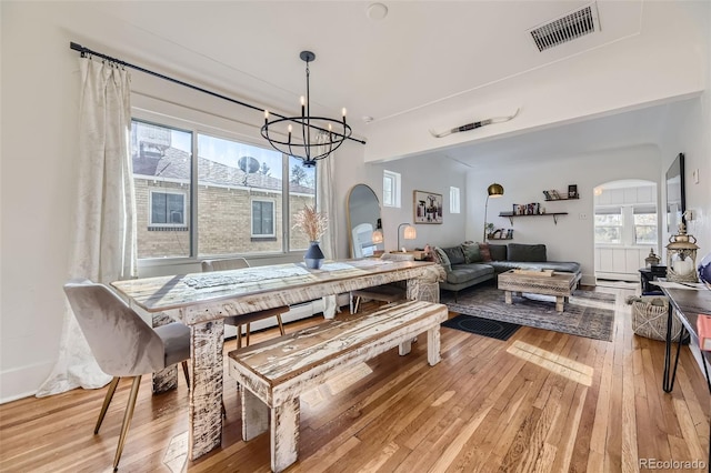 dining room featuring arched walkways, a notable chandelier, visible vents, and light wood-type flooring