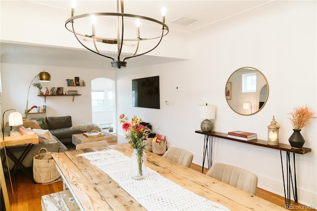 dining room with arched walkways, a notable chandelier, visible vents, and wood finished floors