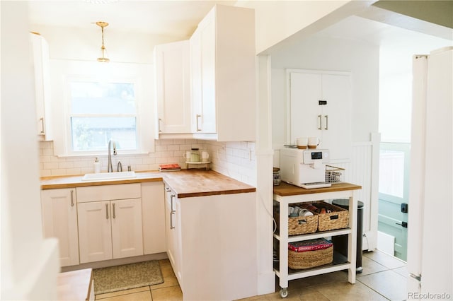 kitchen with white cabinets, light tile patterned flooring, a sink, butcher block countertops, and backsplash