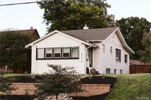 bungalow-style house with fence, a front yard, a chimney, brick siding, and a shingled roof