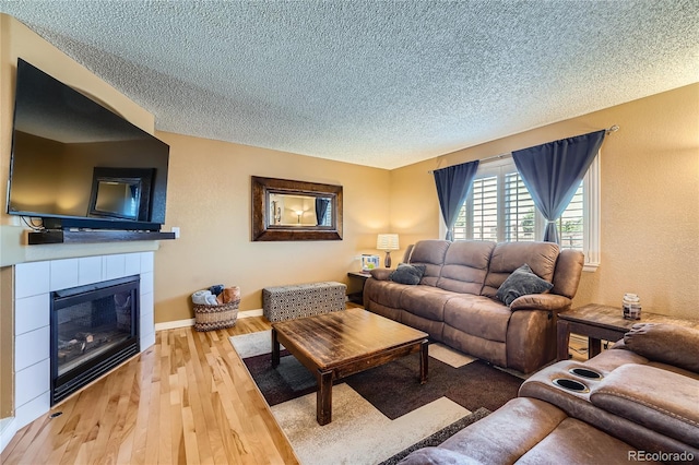 living area with a textured ceiling, a tiled fireplace, baseboards, and wood finished floors