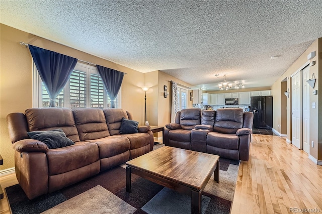 living area with baseboards, a notable chandelier, light wood-style flooring, and a textured ceiling