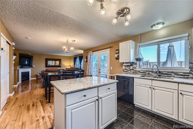 kitchen featuring black dishwasher, white cabinets, open floor plan, a fireplace, and a sink