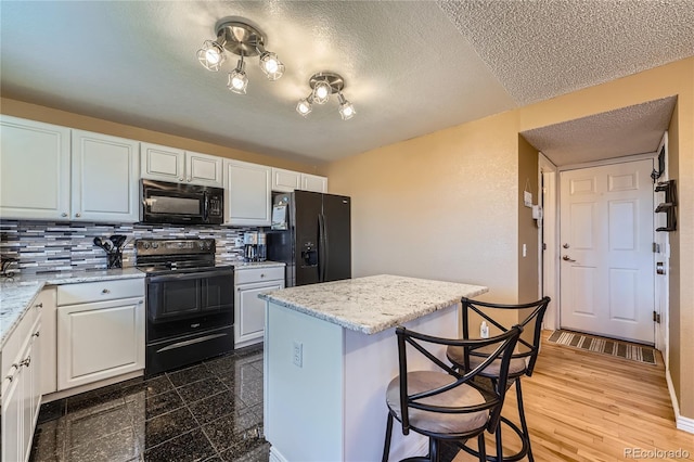 kitchen featuring white cabinets, a breakfast bar, a center island, light stone countertops, and black appliances