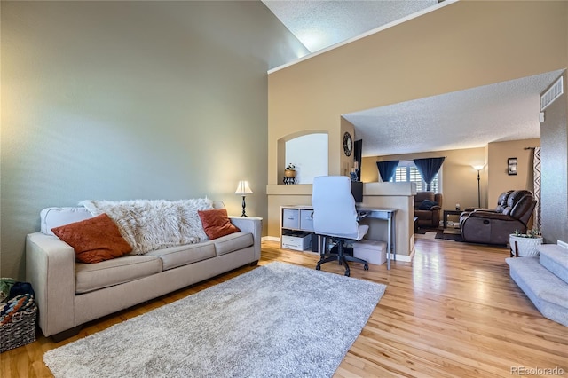 living area featuring visible vents, a towering ceiling, a textured ceiling, wood finished floors, and baseboards