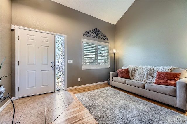 entryway featuring light wood-style floors, baseboards, and vaulted ceiling