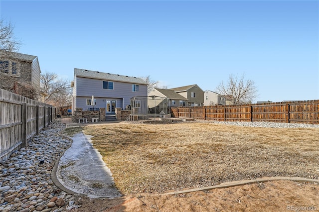 back of property with a patio area, a fenced backyard, a trampoline, and a yard